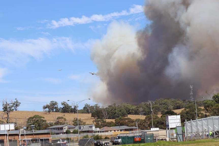 A waterbombing aircraft flies over a fire burning near houses.