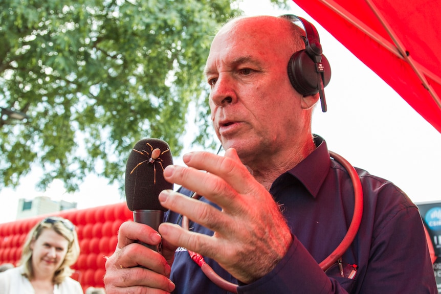 Dr Robert Raven wearing headphones and holding a microphone with a golden orb spider on it at South Bank.