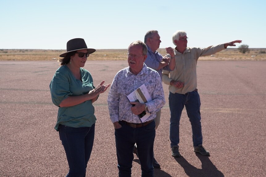 A woman and a man speak while two other men stand behind among bare ground