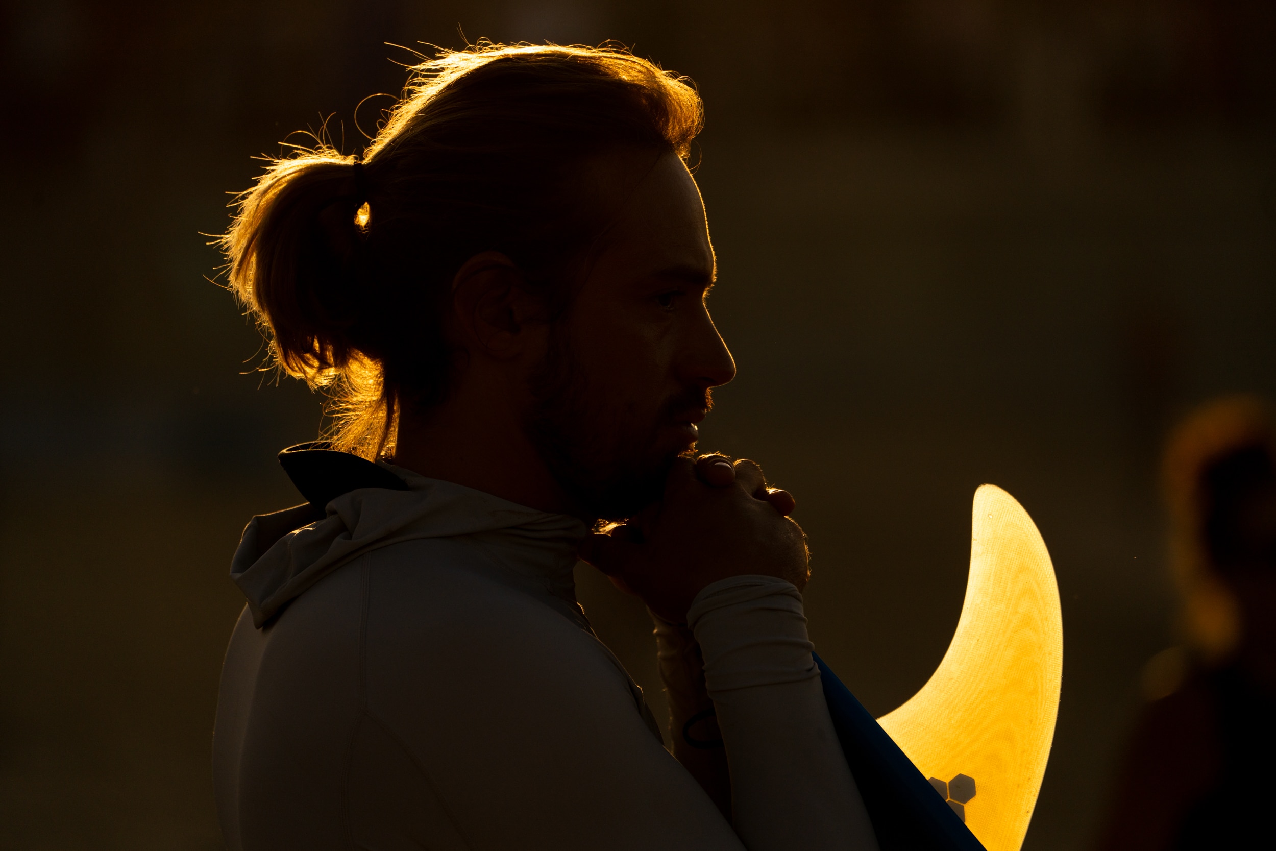 Un hombre sostiene su tabla de surf y el sol brilla sobre él.