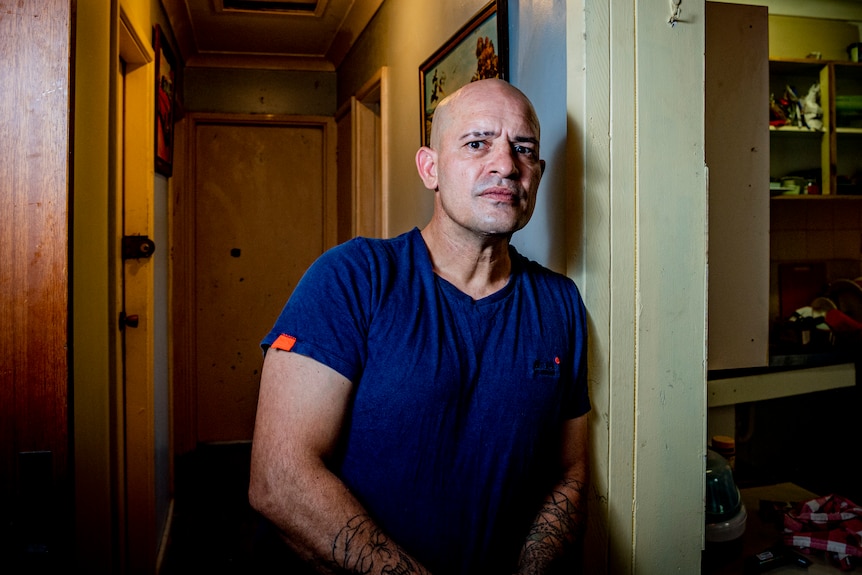 Man wearing a blue shirt leaning against a wall in a hallway.