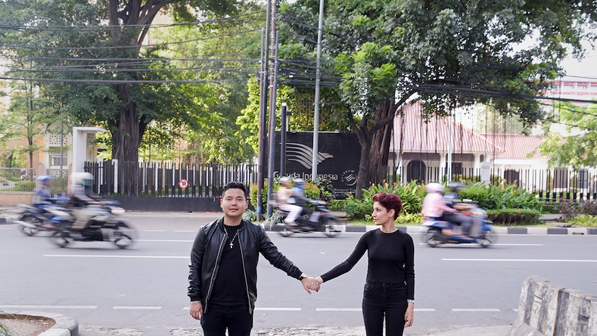 Pasangan berpegangan tangan di pinggir jalanan sibuk