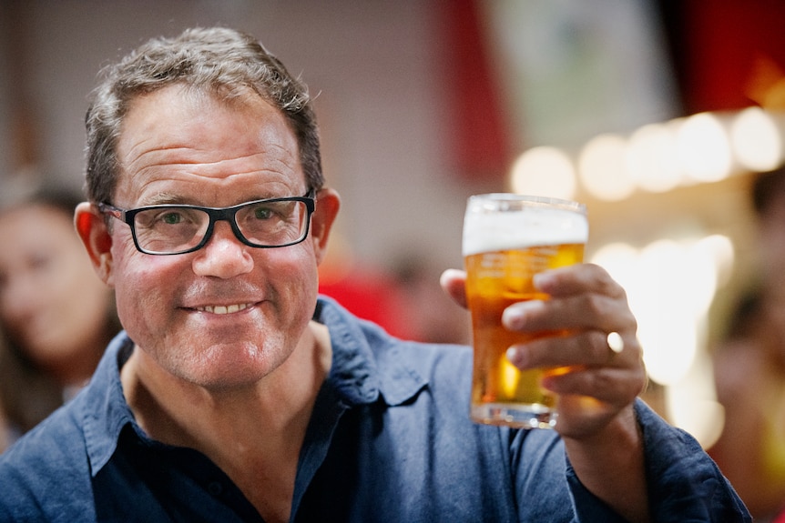 A man smiling and raising his beer at the camera.