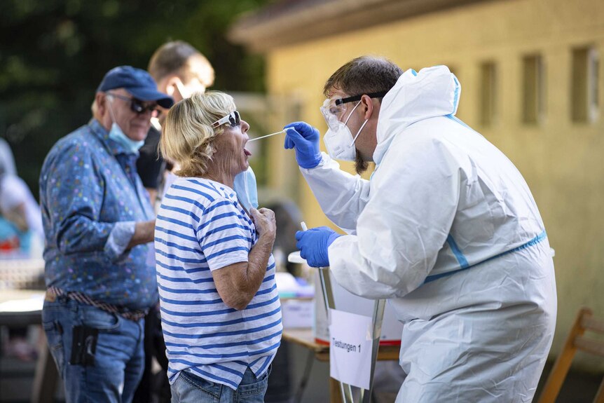 A person in a hazmat suit swabs the mouth of a woman