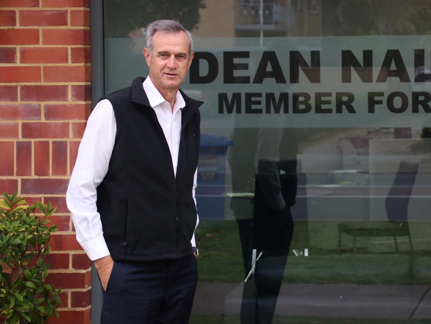 Tony Simpson stands in front of a glass window with Dean Nalder's name in front.