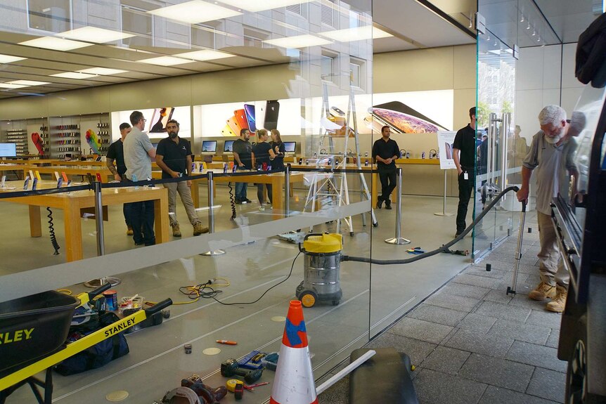 A wide shot showing people inside the Apple Perth City store as a  man with a vacuum cleaner cleans up at the entrance.