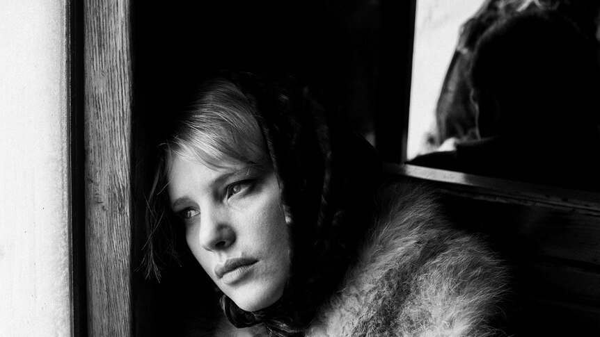 Black and white still of Joanna Kulig looking out window in foreground, young girl in background in 2018 film Cold War.