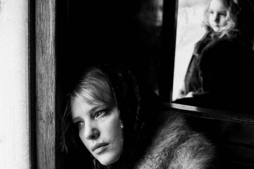 Black and white still of Joanna Kulig looking out window in foreground, young girl in background in 2018 film Cold War.