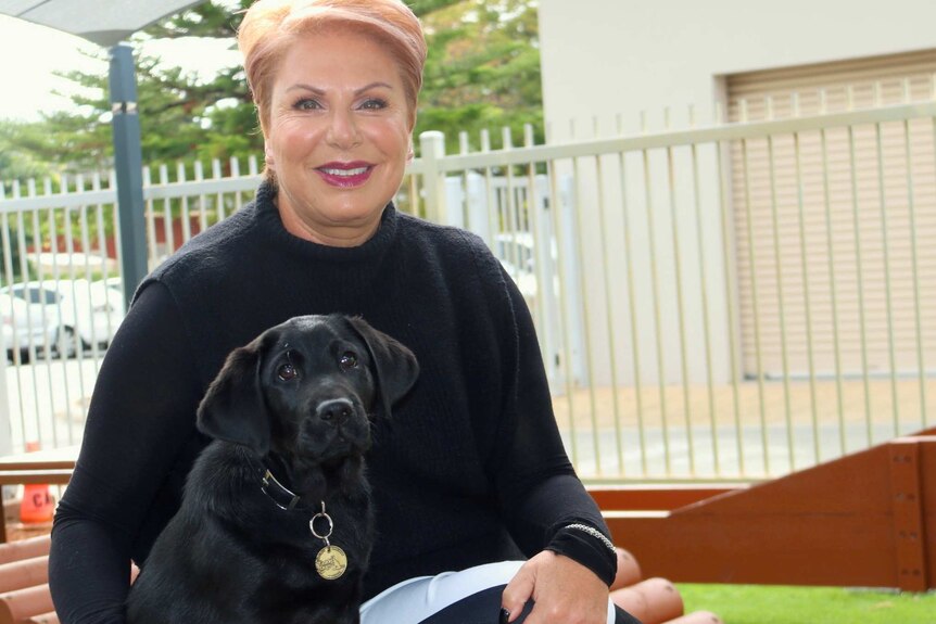 Debra Schaffer sits outdoors posing for a photo with black guide dog puppy Comet.