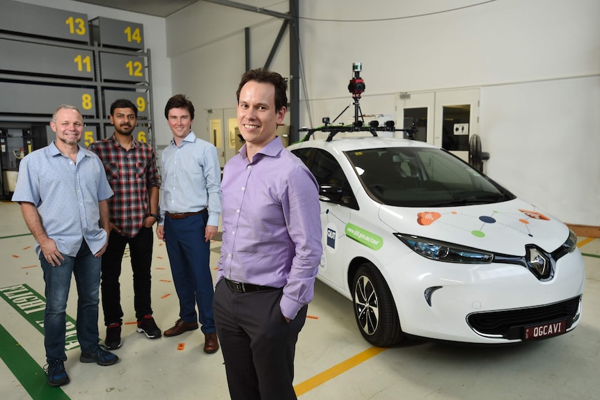 four men stand beside a self-driving car prototype in a large garage