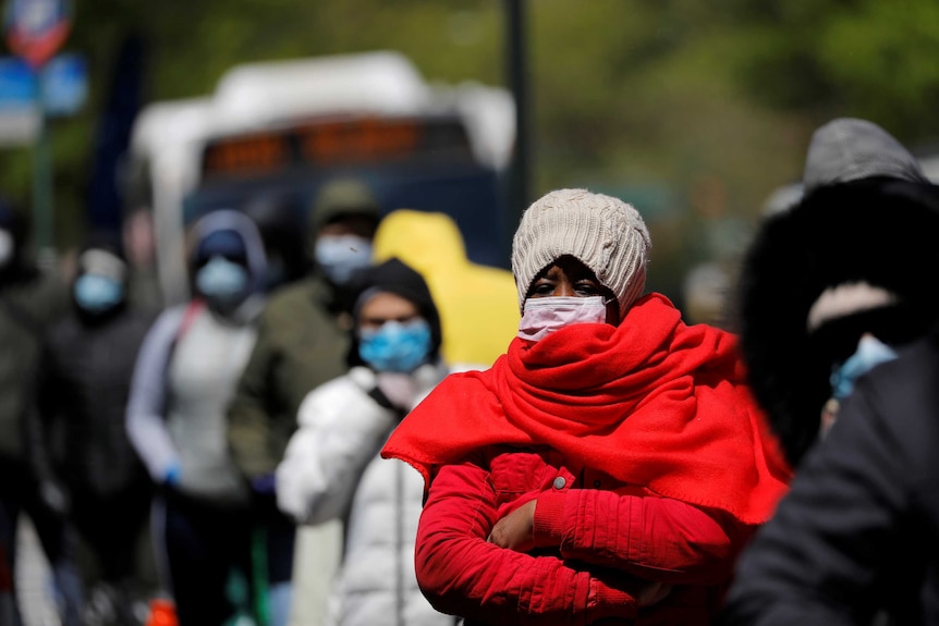 A woman in a face mask in a line of other people also wearing masks