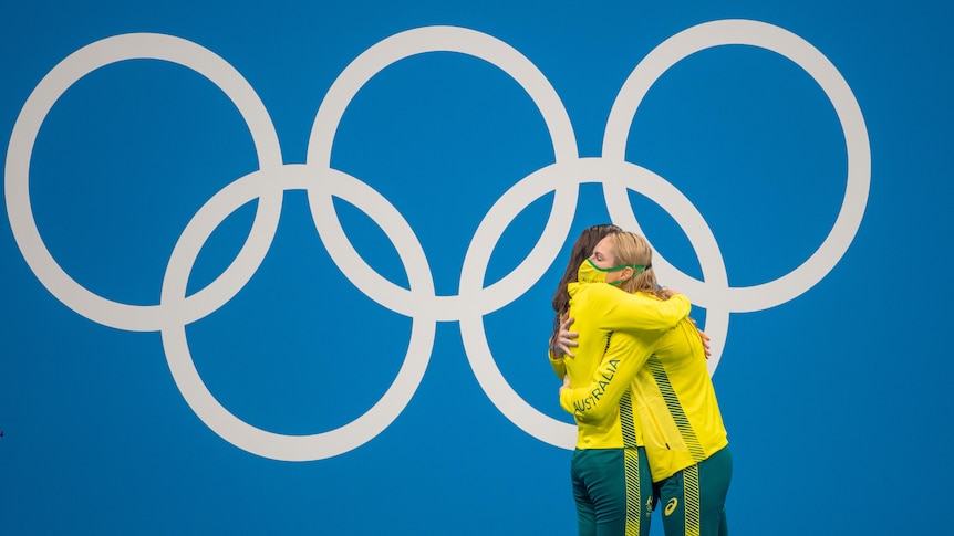 Australian swimmers Emily Seebohm and Kaylee McKeown hug on the dais at the Tokyo Olympics, with the Olympic rings behind them.