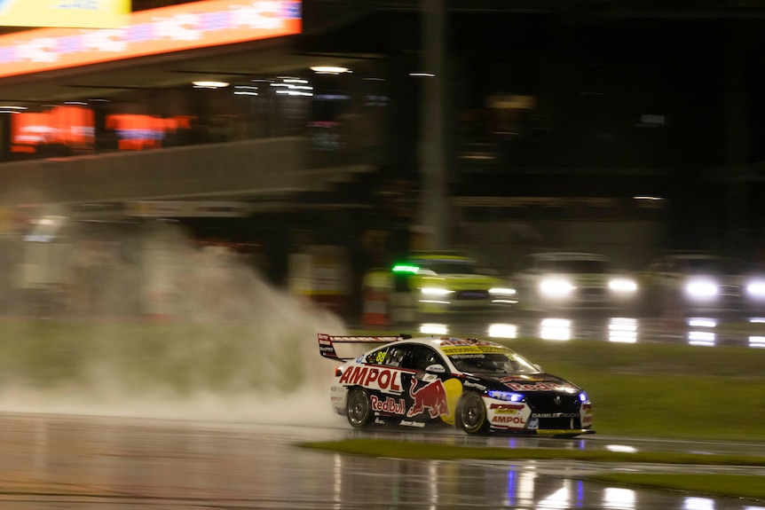 A yellow and blue car generates a big puddle on a rain-soaked racing track at night