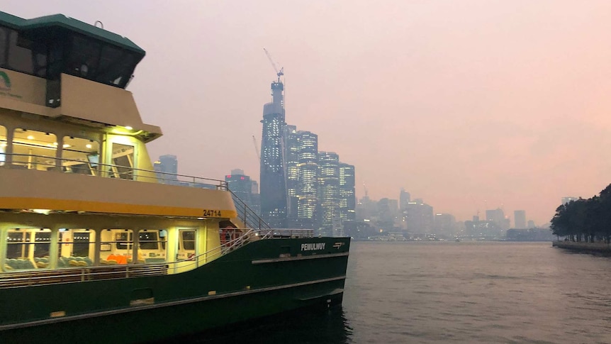 A ferry sets off from a wharf in front of a smoke city ckyline.