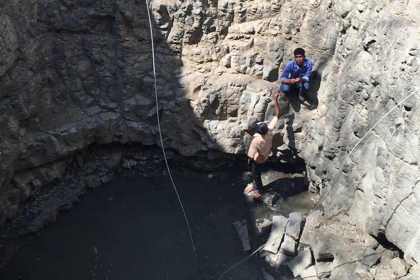 Villagers retrieve water from the bottom of a murky well.