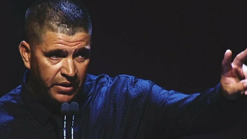 Jeffery Amatto speaking in front of a microphone with an arm outstretched