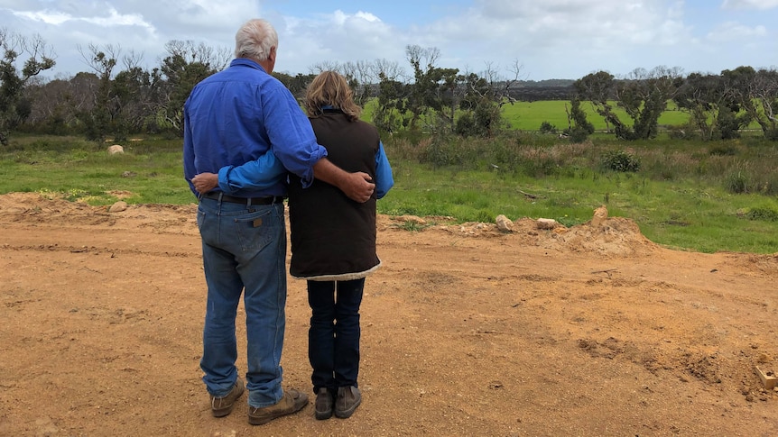 A couple are arm in arm, looking out on the view of green trees