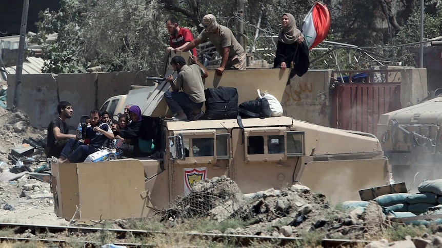 Iraqi security forces transport displaced civilians with an armoured fighting vehicle.