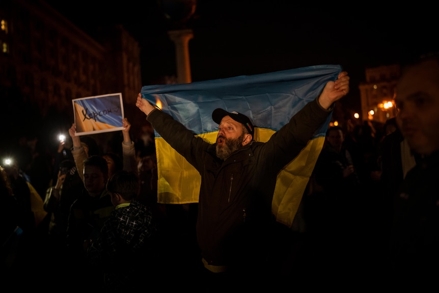 A man holds aloft a Ukranian flag while walking during the night.
