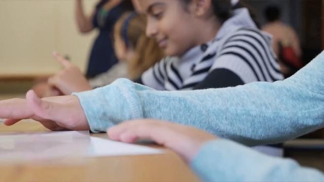 Child's hands in foreground, young girl sits in background