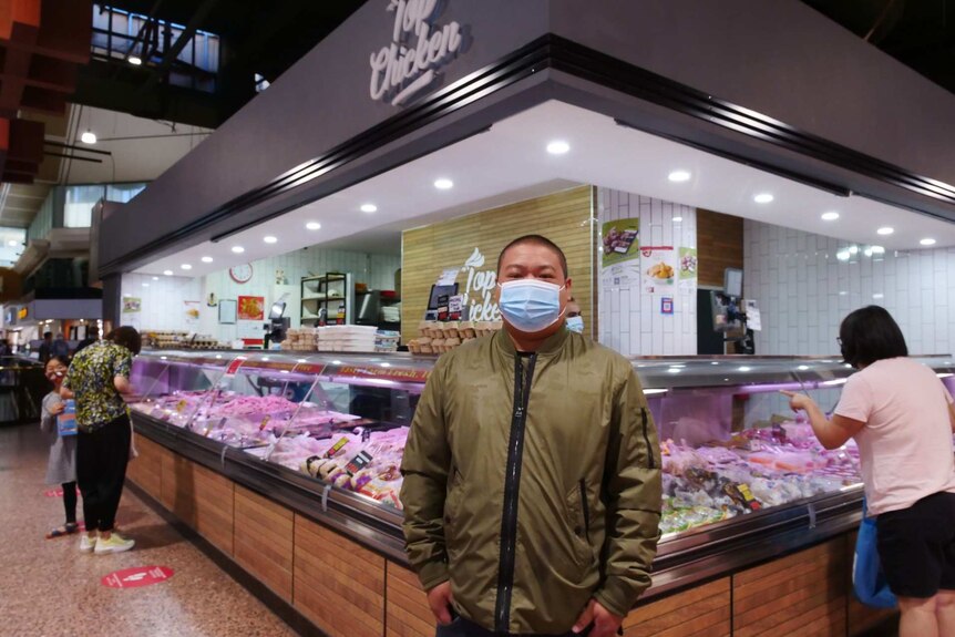 An Asian man with a mask on stands in front of a chicken show in a suburban shopping centre