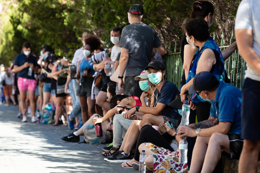 Long lines of people wearing face masks wait to be tested for COVID-19.