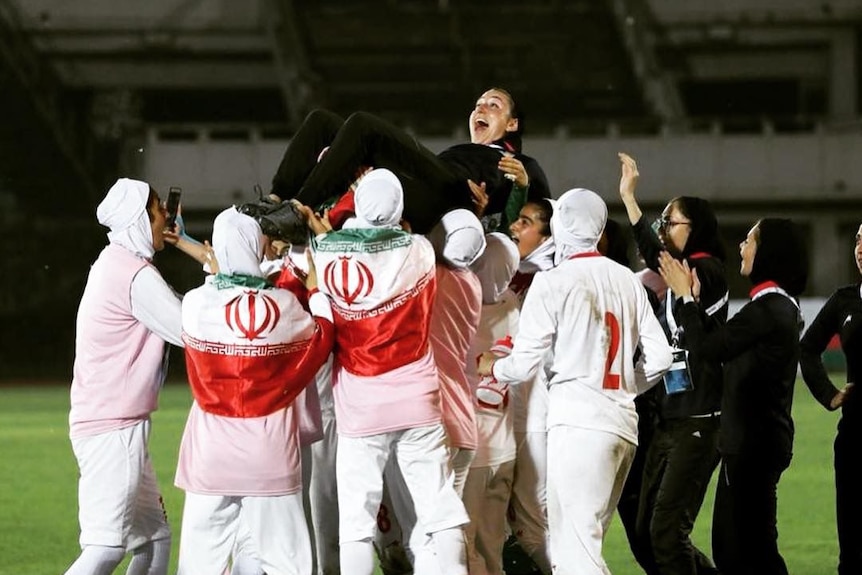 A football team celebrates a result, lifting up their head coach into the air