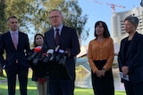 A man and three women stand behind anthony albanese speaking into the microphone