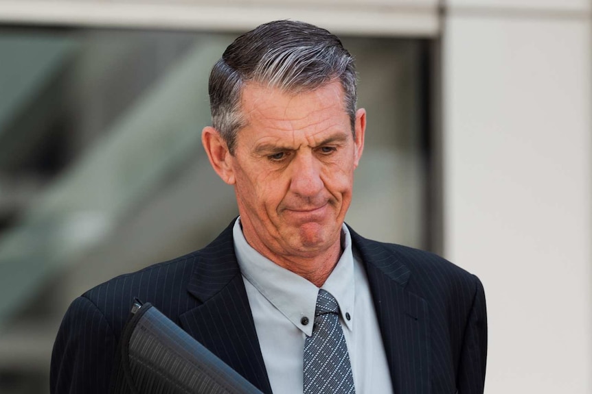 A man in a suit holding a black folder outside court.