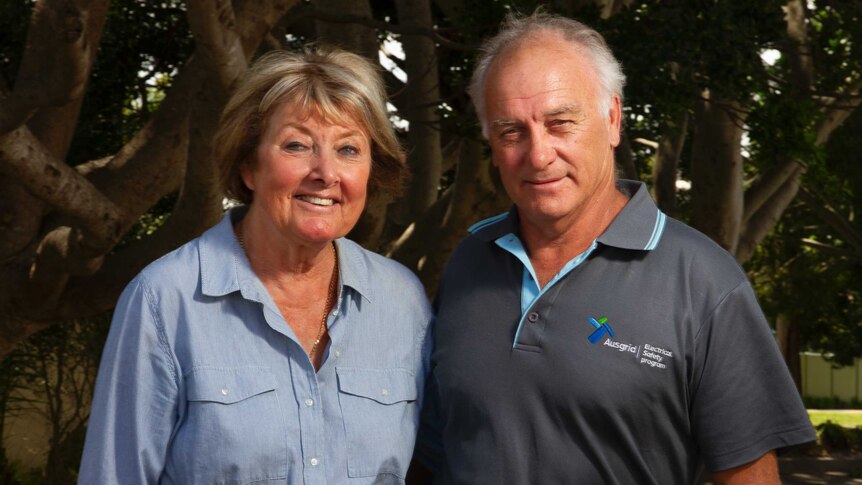 A woman and a man standing close together beneath a canopy of trees in a school playground.