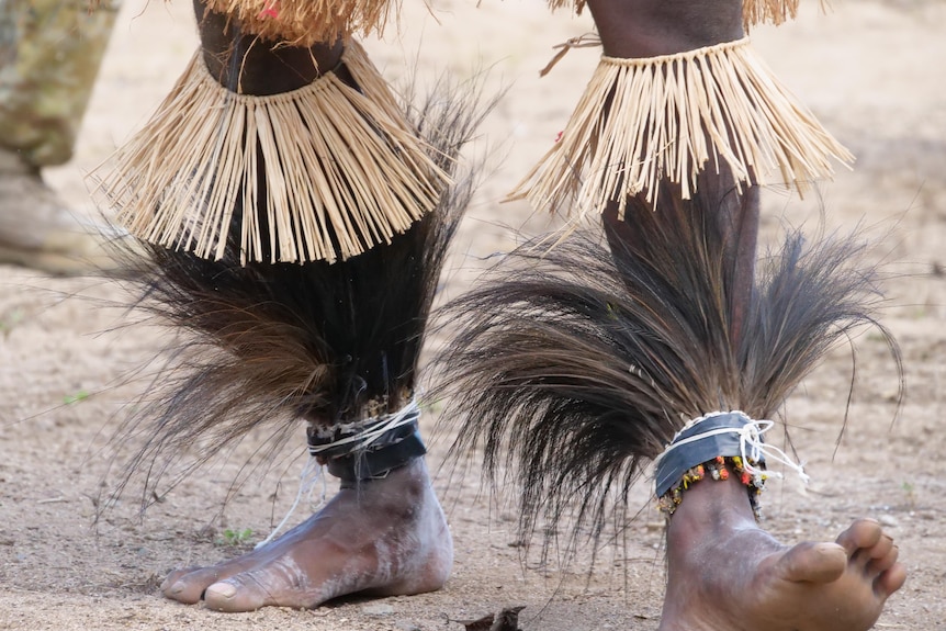 Close up of Torres Strait Islander man's feet adorned with feathers dancing on sand