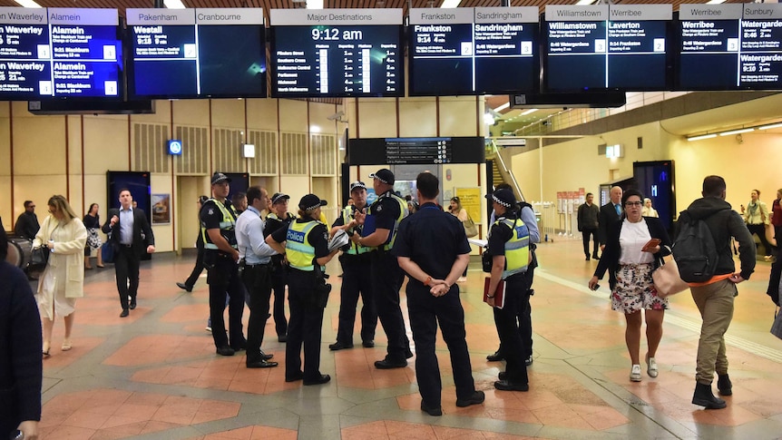 Police on the concourse of Flagstaff station under destination timetable screens.
