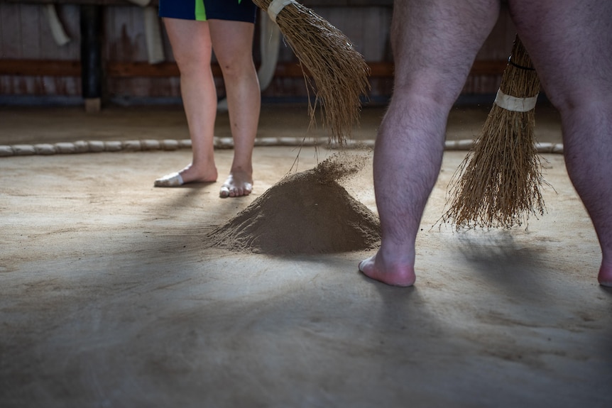 Two people sweeping a dirt circle 