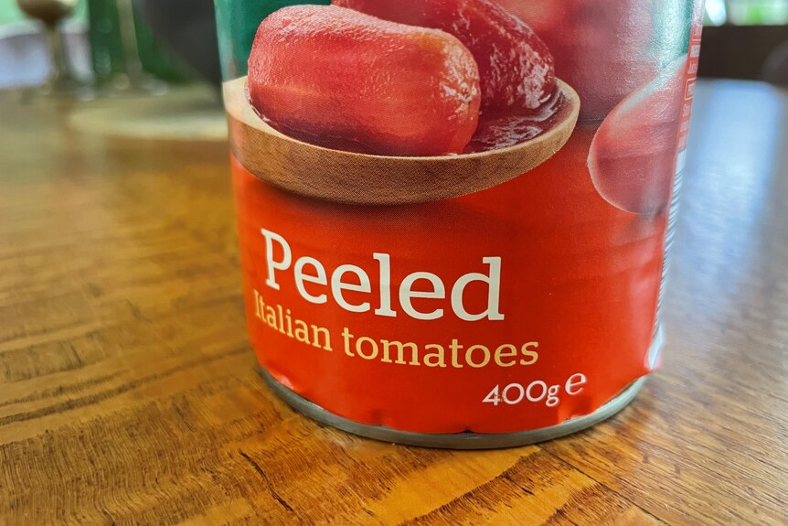 Close up of canned tomatoes on a silky oak wood table. 
