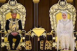 Close up of Malaysia's new king and queen wearing elaborate clothes and sitting on thrones