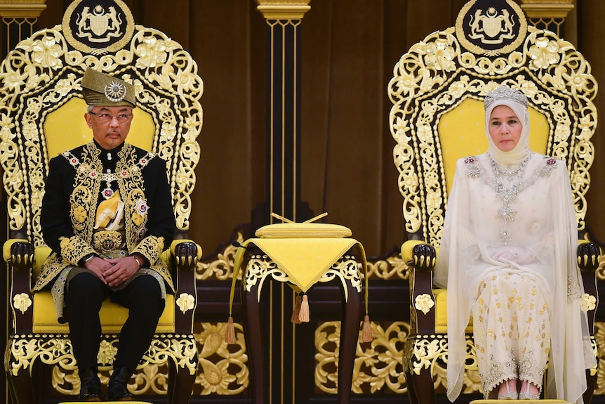 Close up of Malaysia's new king and queen wearing elaborate clothes and sitting on thrones