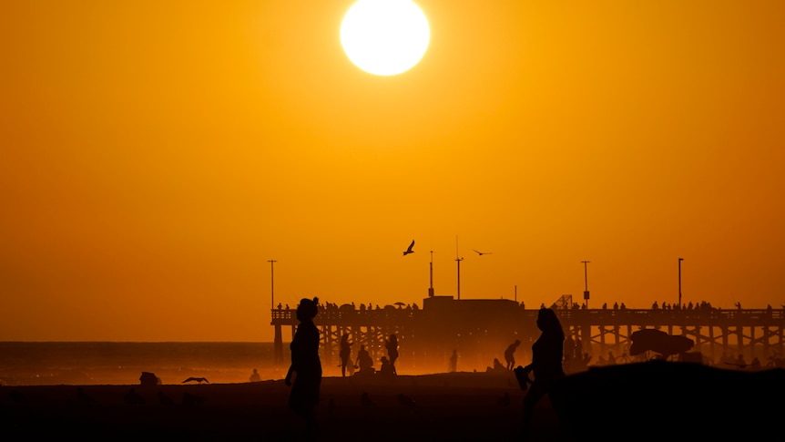 Beachgoers walk along the waterfront as the sun sets