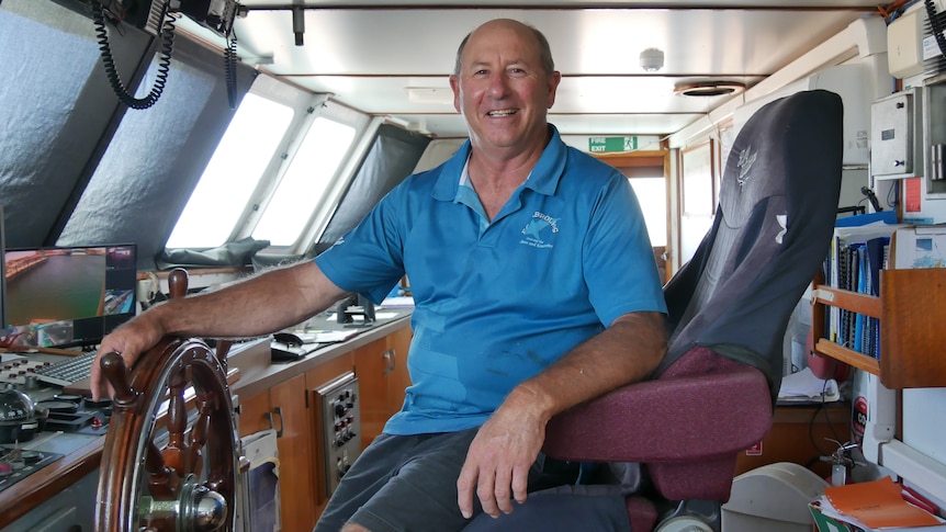 Man in blue shirt sits inside the cabin of a boat.