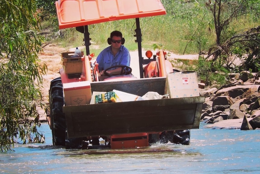 A tractor driving through floodwater with supplies in it