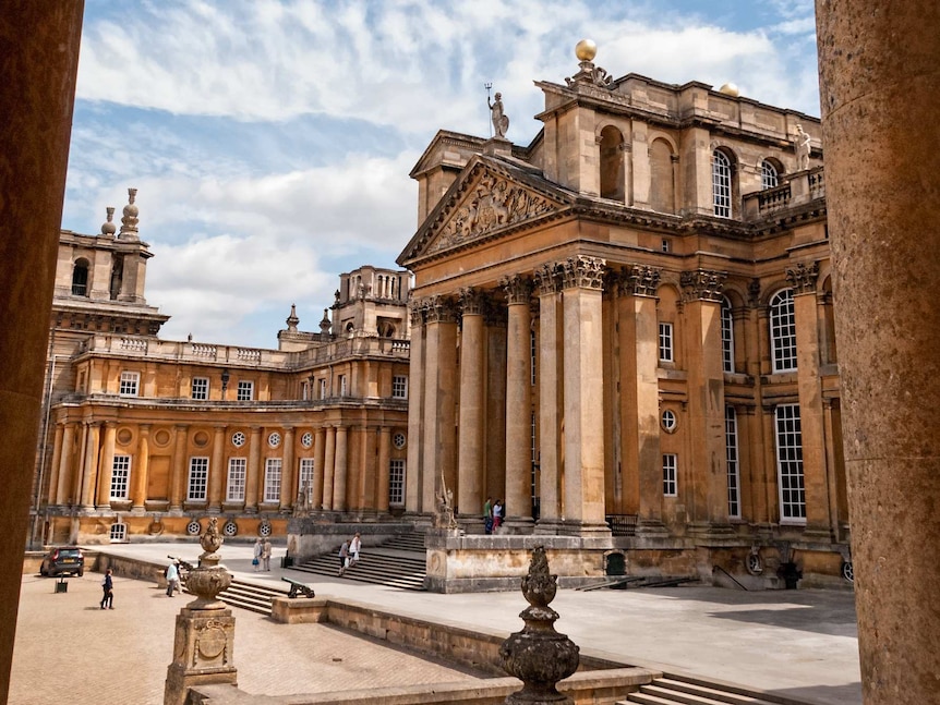 An ornate Georgian palace is seen through two classical columns on a sunny day.