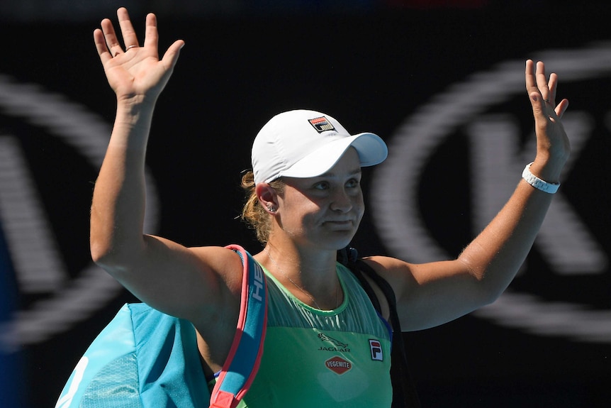 A glum-looking tennis player holds her hands up to salute the crowd after losing a match.
