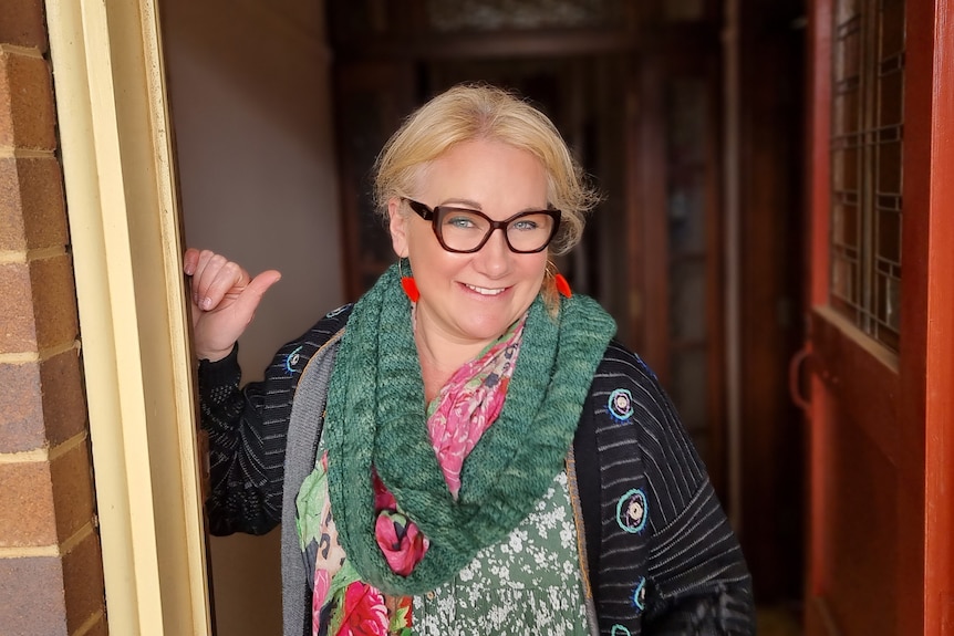 Woman with blonde hair and glasses standing at a doorway.