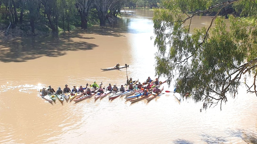 A group of kayakers together in a group on a river with brown water