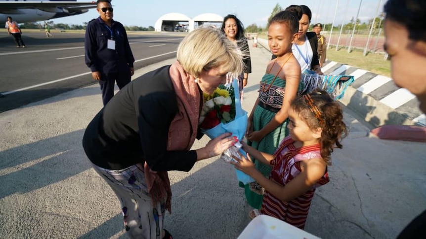 Julie Bishop leans down to accept flowers from a young girl.