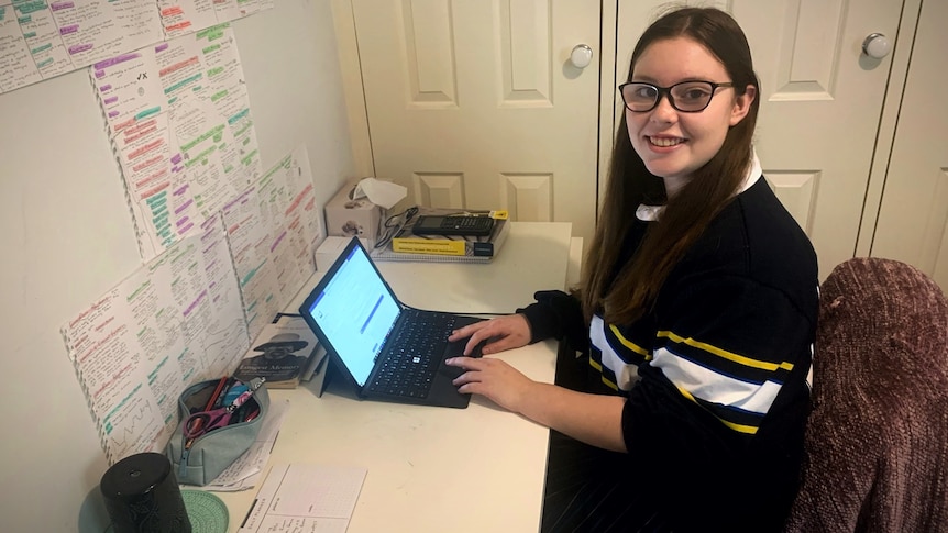 A student sits working at her laptop,  the wall is covered with colour coordinated notes