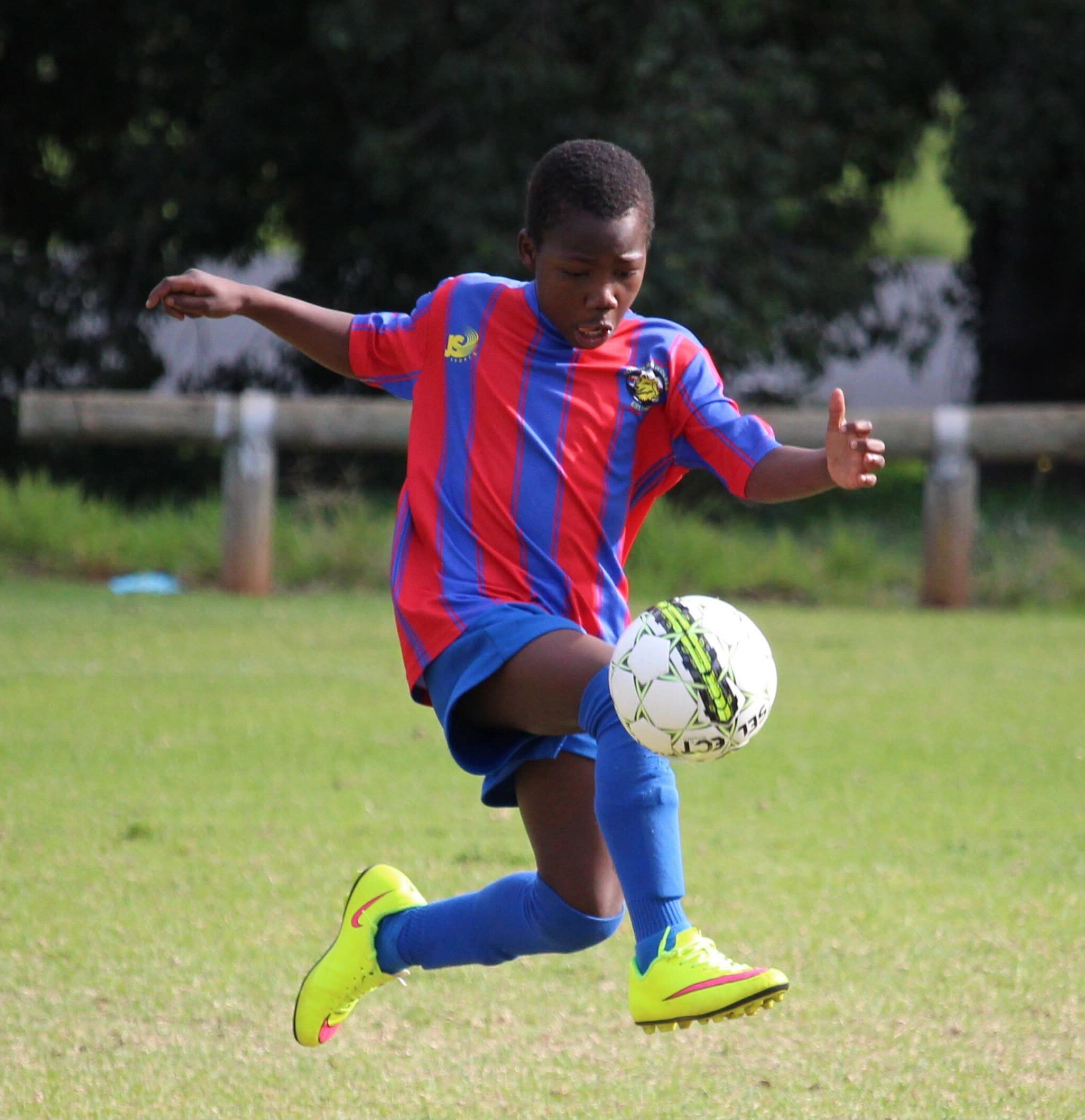 A child wearing a soccer uniform is kicking a soccer ball.