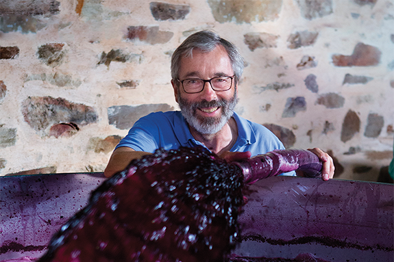 A man stands behind a large vat of purple red wine