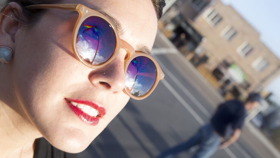 The LGBT pride flag is reflected in a woman's sunglasses.
