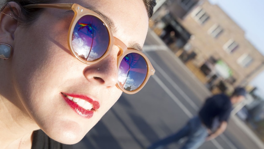The LGBT pride flag is reflected in a woman's sunglasses.