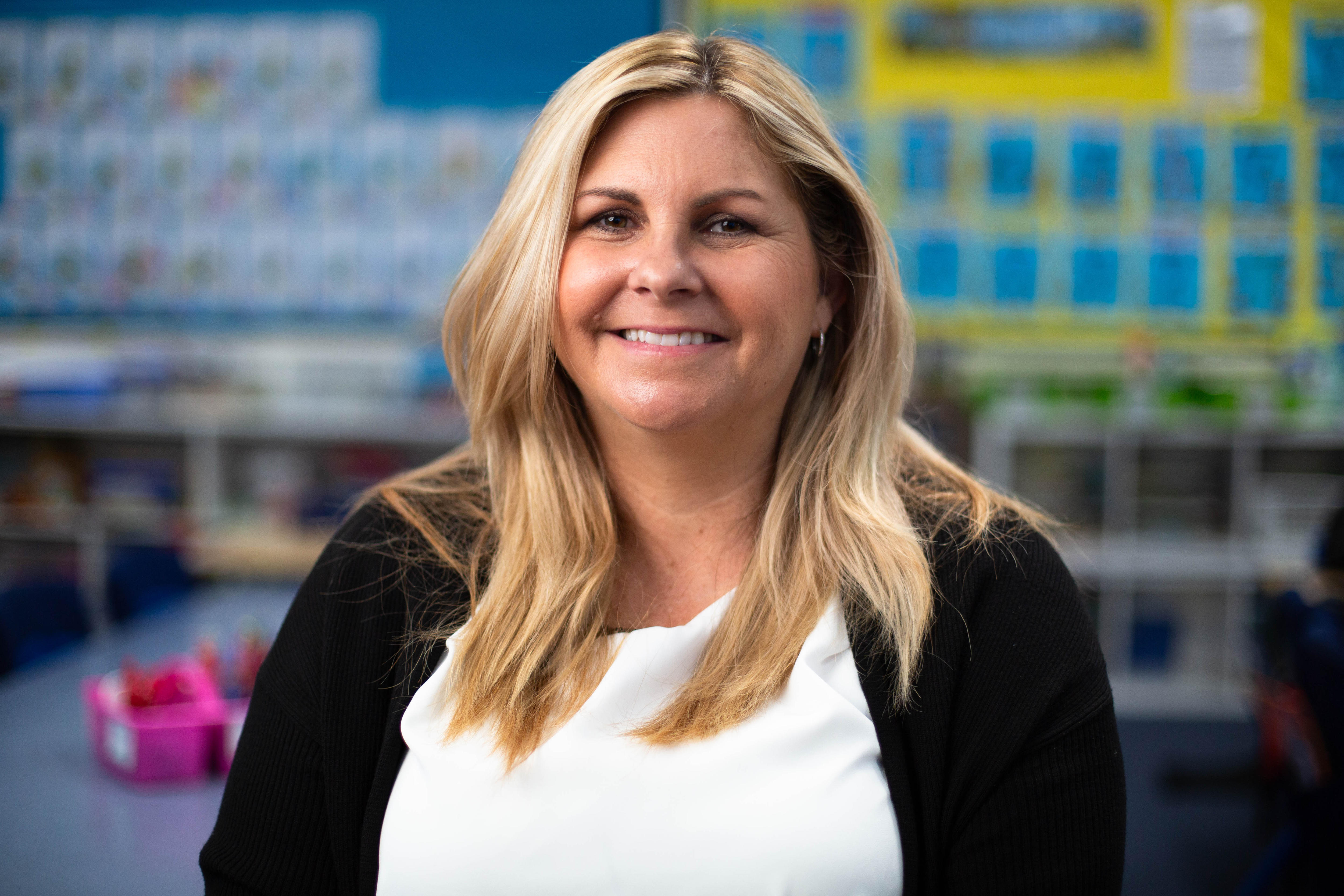 A young blonde, white woman smiling in a clasroom